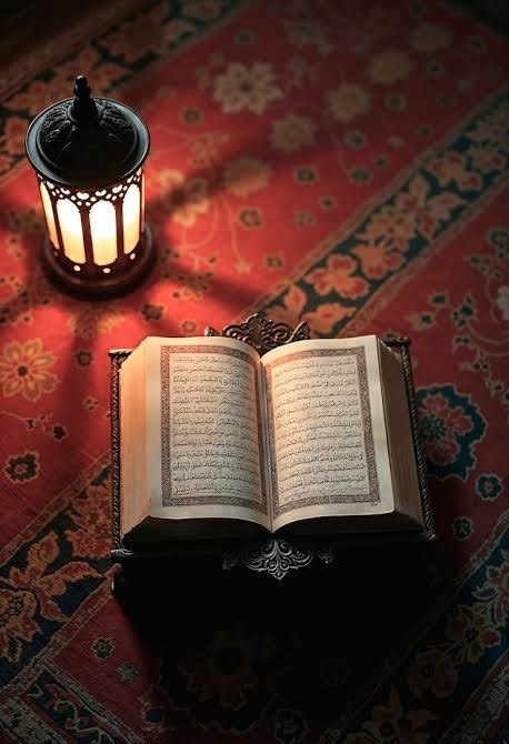 Holy Quran with lantern on prayer mat spiritual image.
