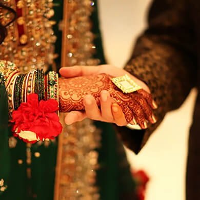 Indian bride and groom holding hands during wedding ceremony with mehndi and red flowers.