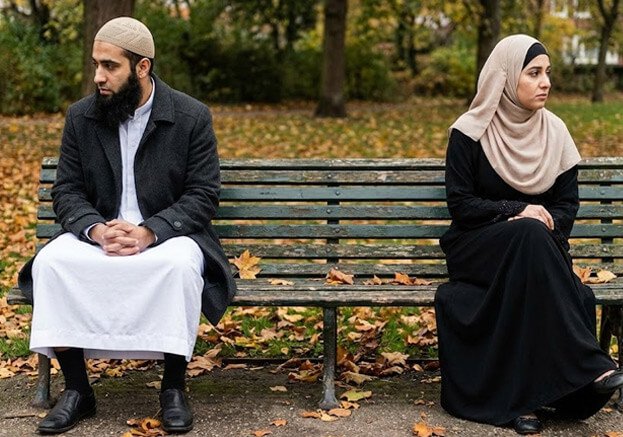 Muslim couple sitting separately on park bench showing relationship distance and sadness.